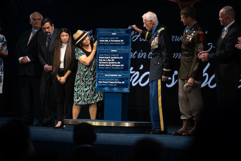 Seven people on a stage look at a large plaque.