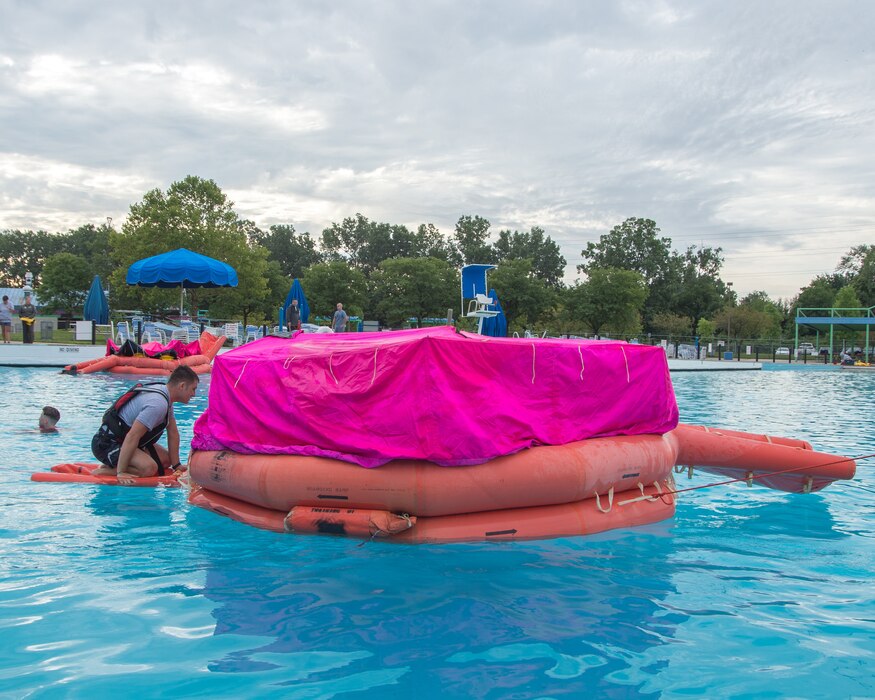 Large life raft floating in pool with pink cover, practicing signaling friendly aircraft.