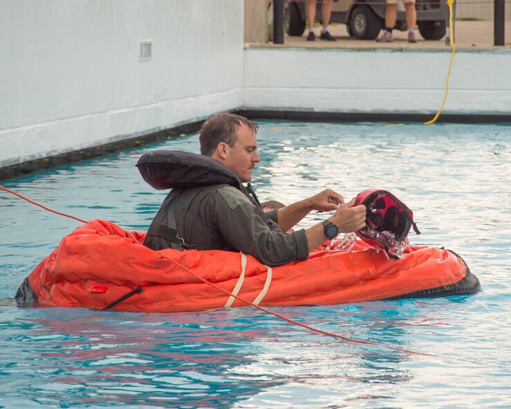 Pilot in small life raft uses helmet to remove water from inside.