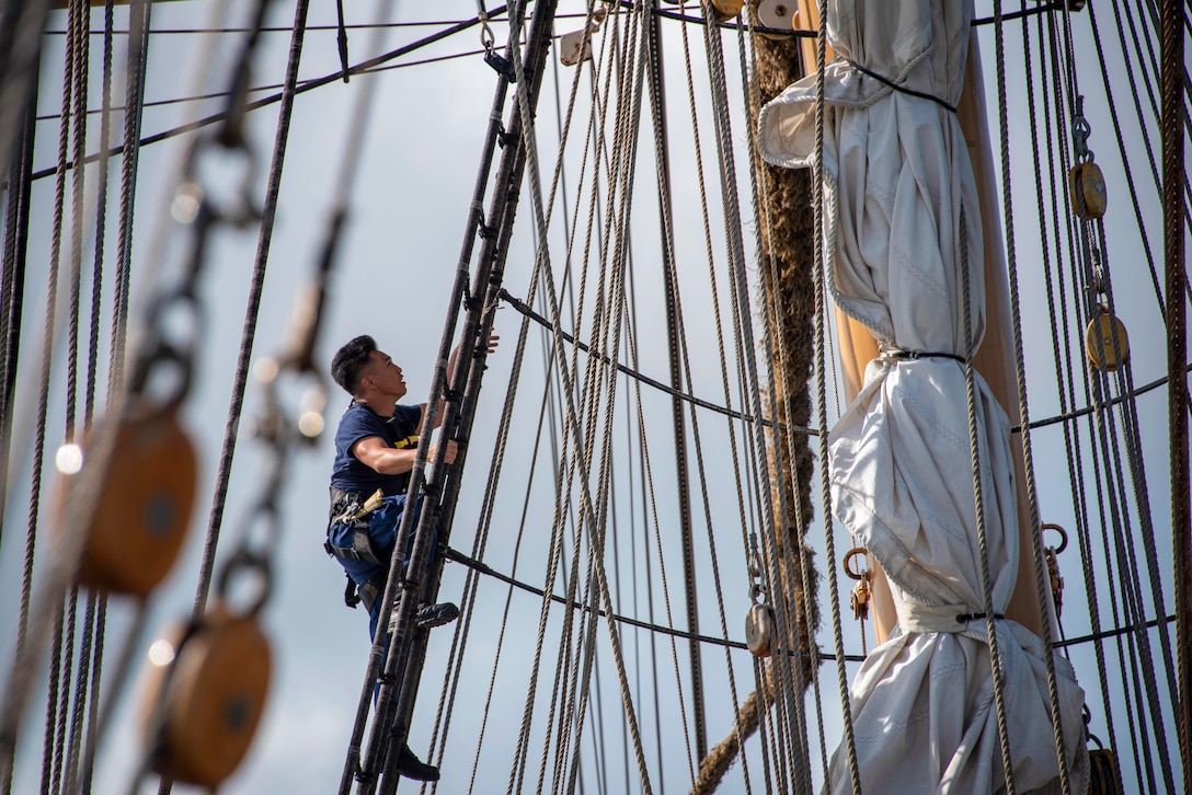 A Coast Guard cadet climbs the rigging aboard a ship.