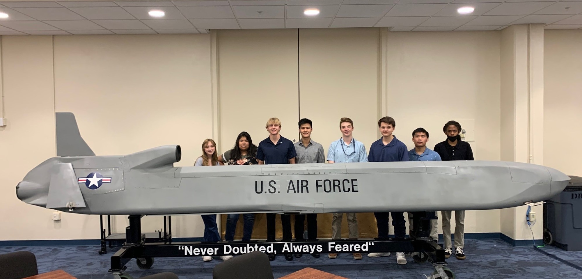 Group of teenagers posing behind of a model cruise missile