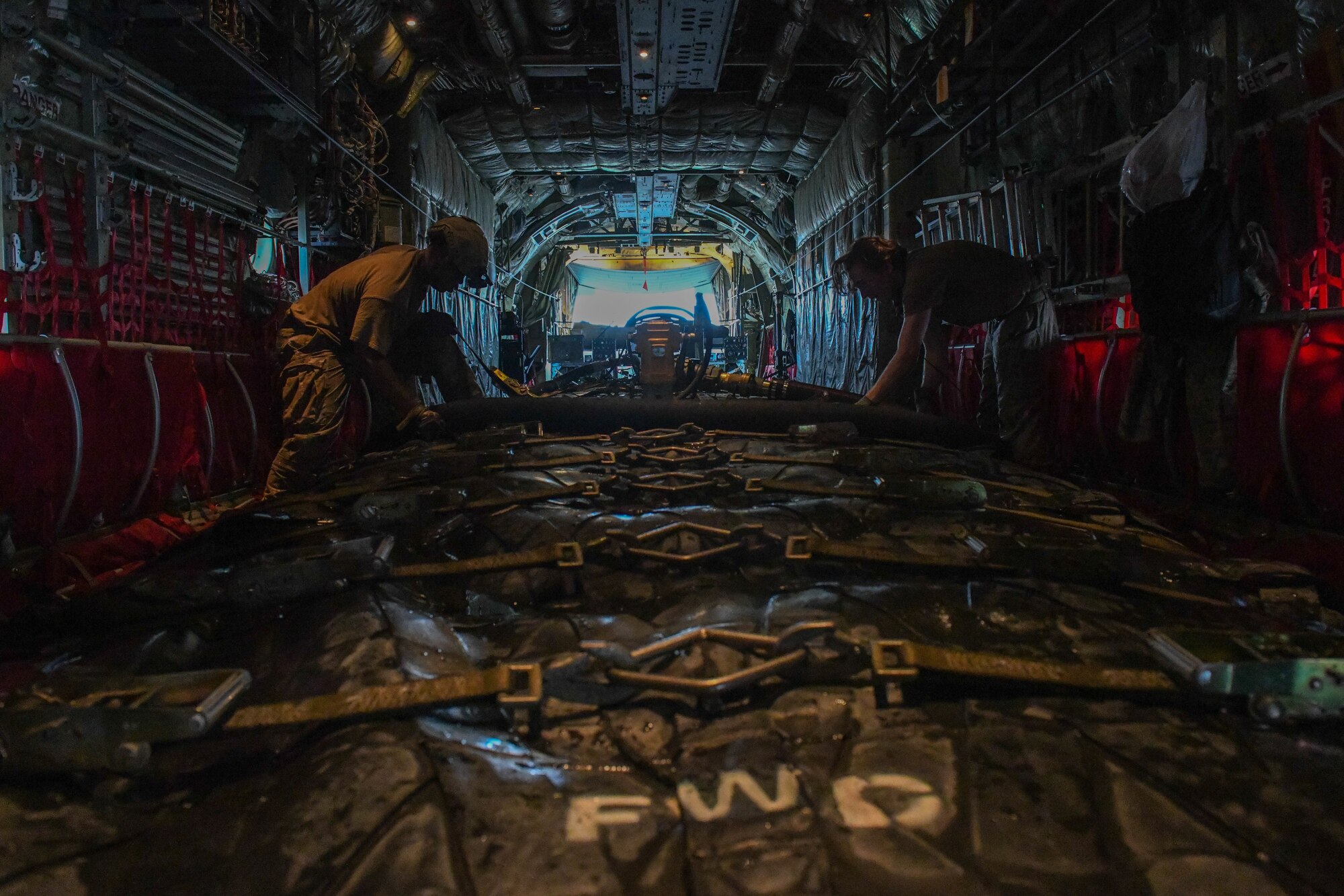 Airmen tighten straps on a fuel bladder aboard a C-130J Super Hercules