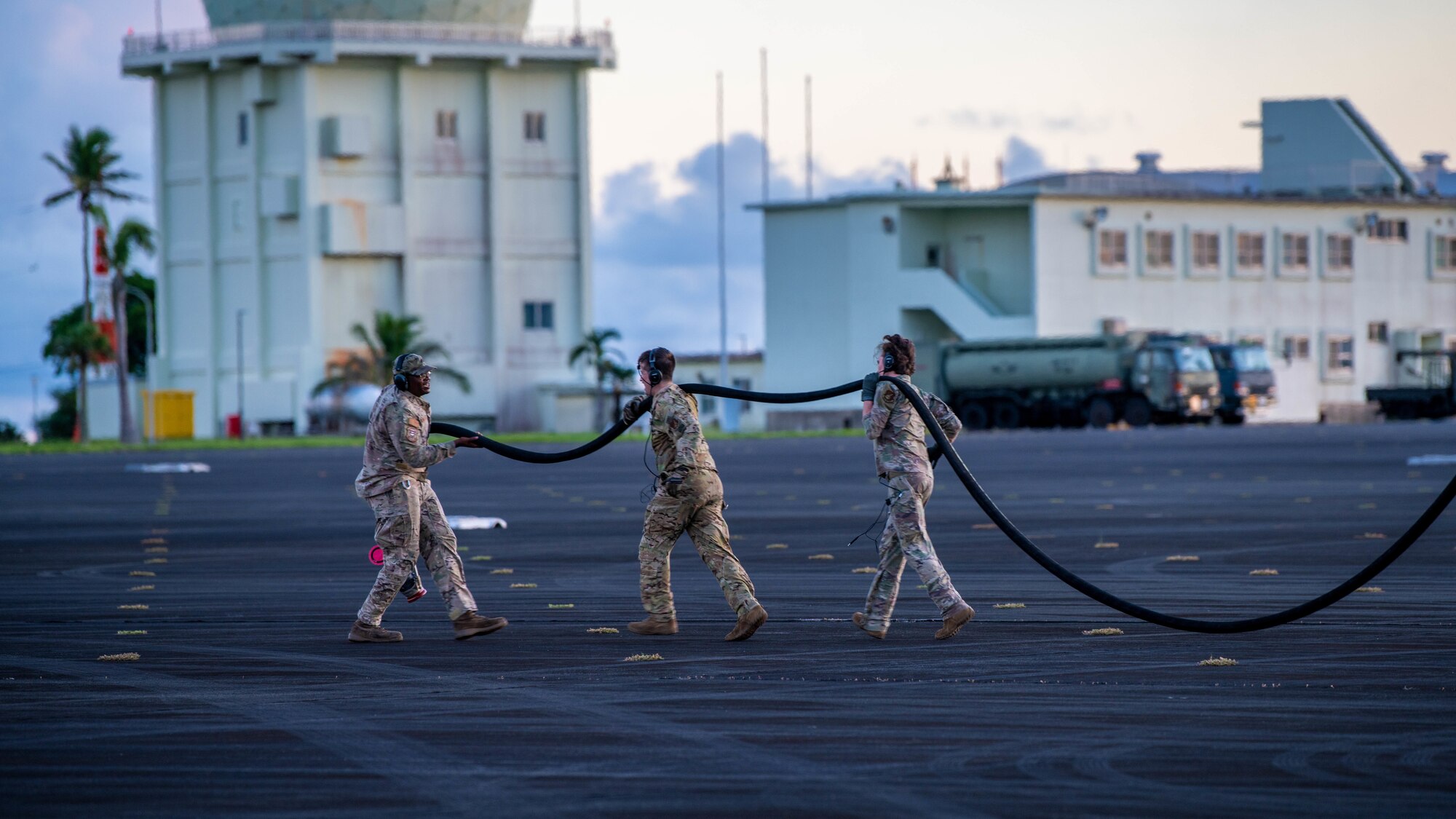 Airmen guide a fuel hose across a flightline