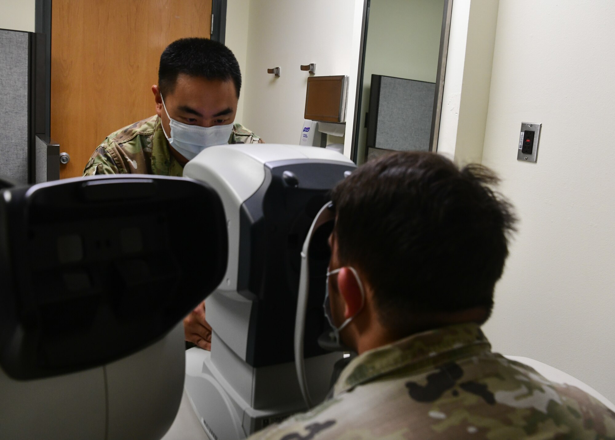 A military member conducts an eye exam on another military member.