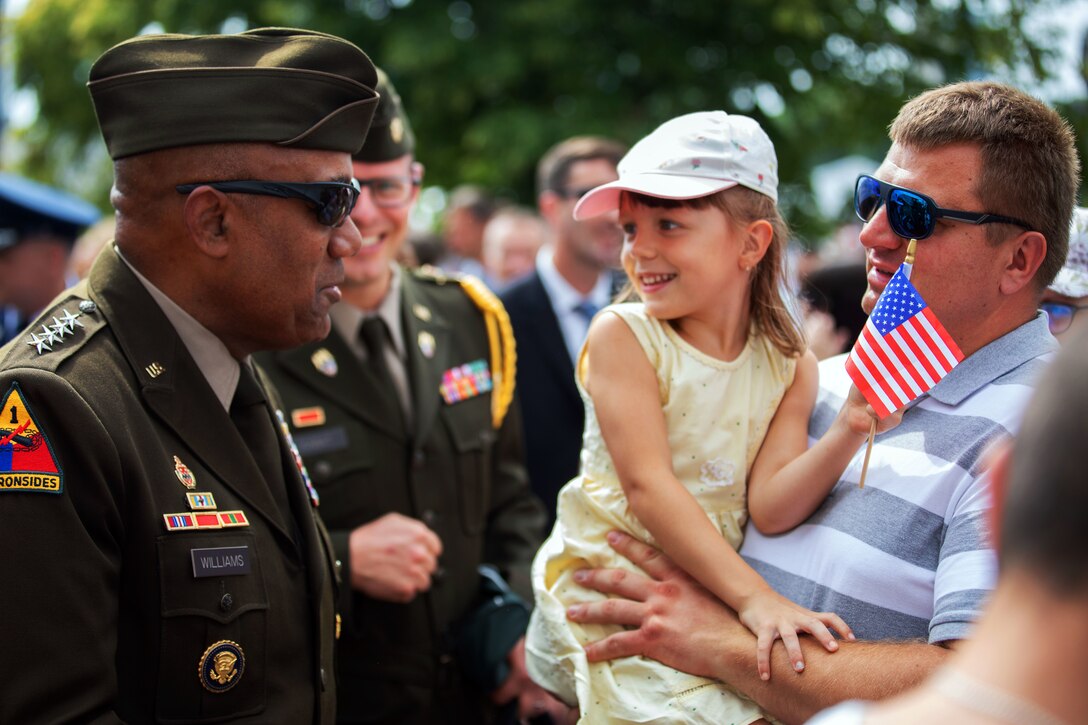 An Army general speaks to a child holding a flag while being held by her father.