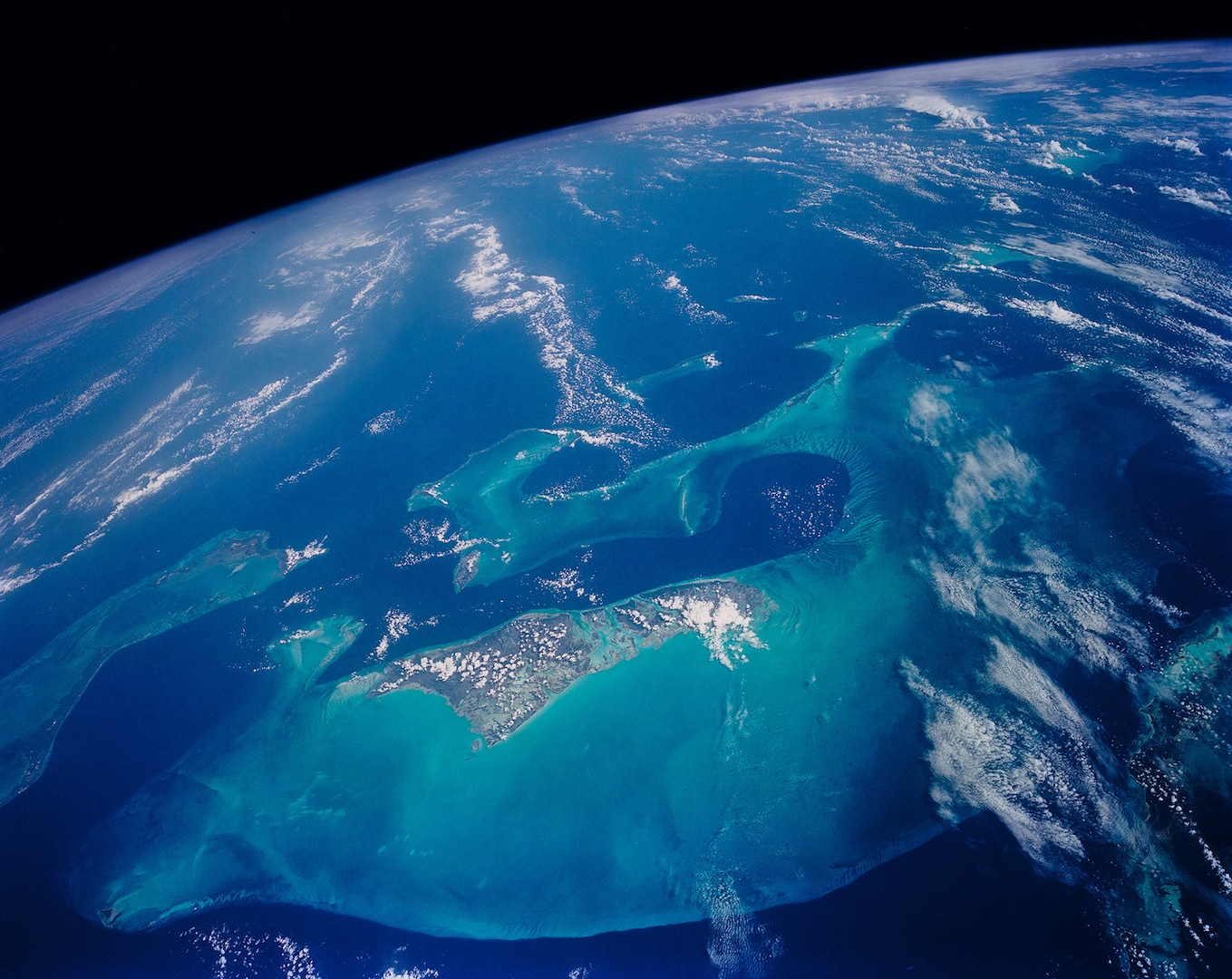 The light blue shallow water platforms of the Bahamas, which are separated by very deep dark blue channels, make for a striking scene. The Bahamas are one of the few regions where calcium carbonate precipitates directly out of the water, as the mineral aragonite, to form the coral reef islands.