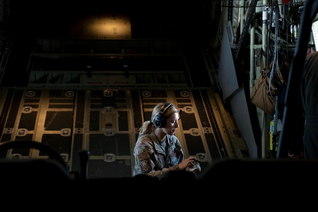 An airman sits on an aircraft while eating.