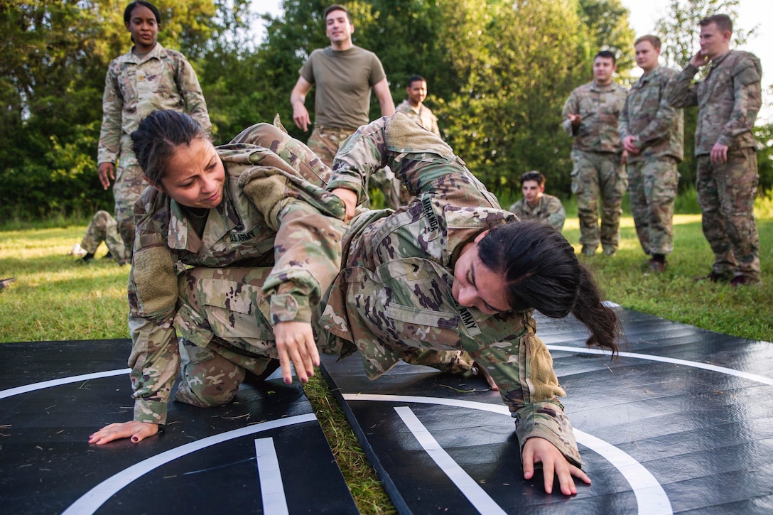 Two soldiers fight on a mat during training as fellow soldiers watch.