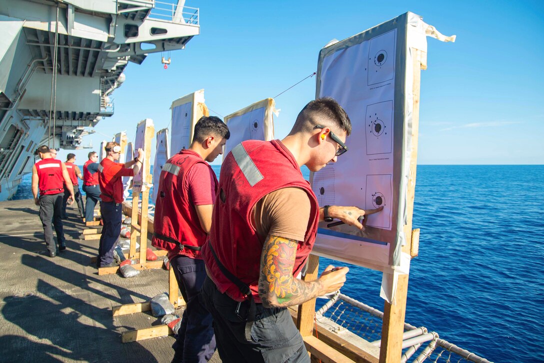 Sailors look at rifle target sheets aboard a ship at sea.
