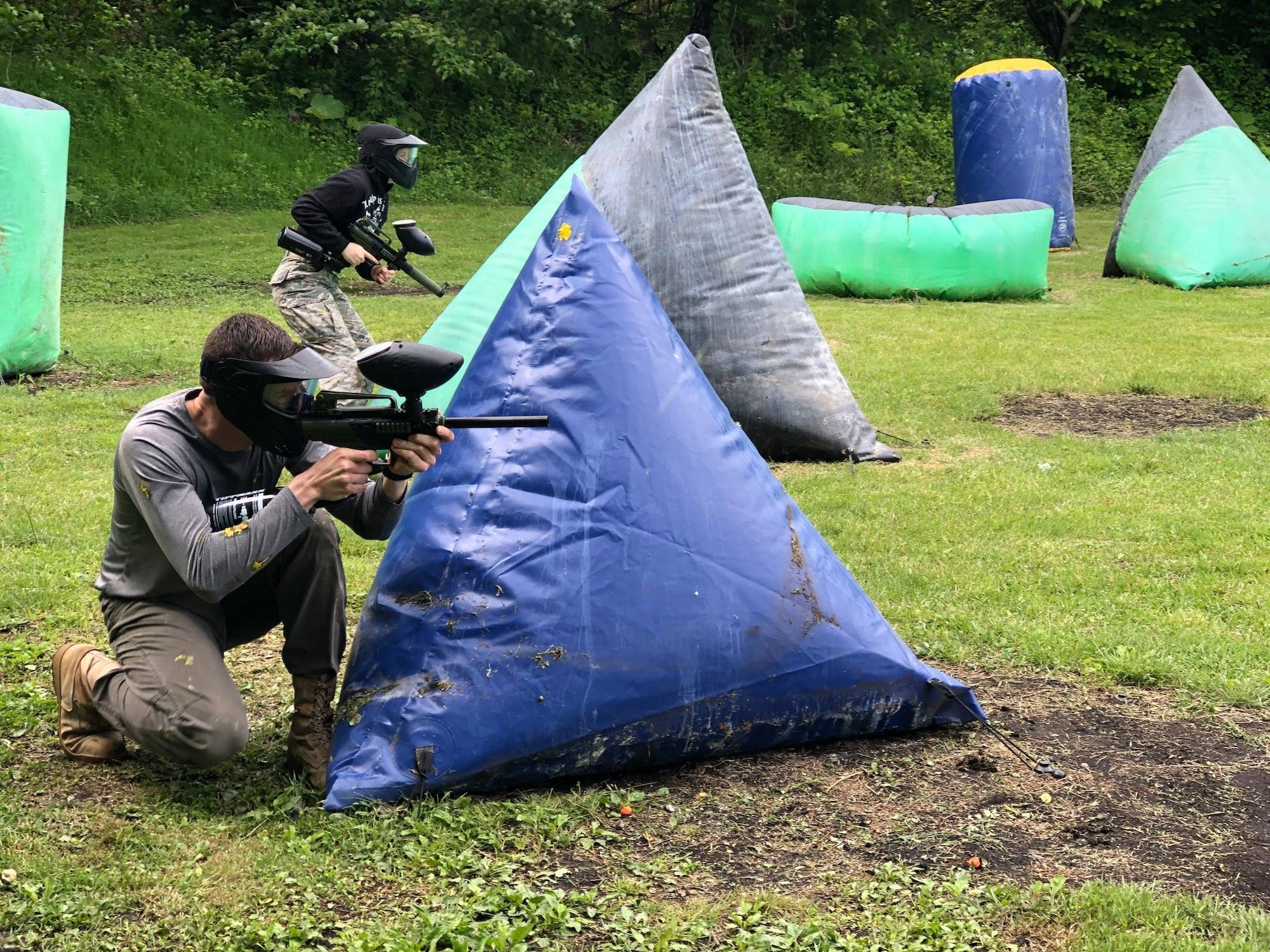 Members shoot a paintball gun while taking cover.
