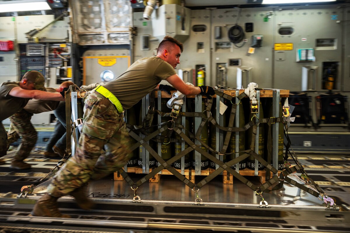 Four airmen push a pallet of ammunition in the cargo hold of an aircraft.