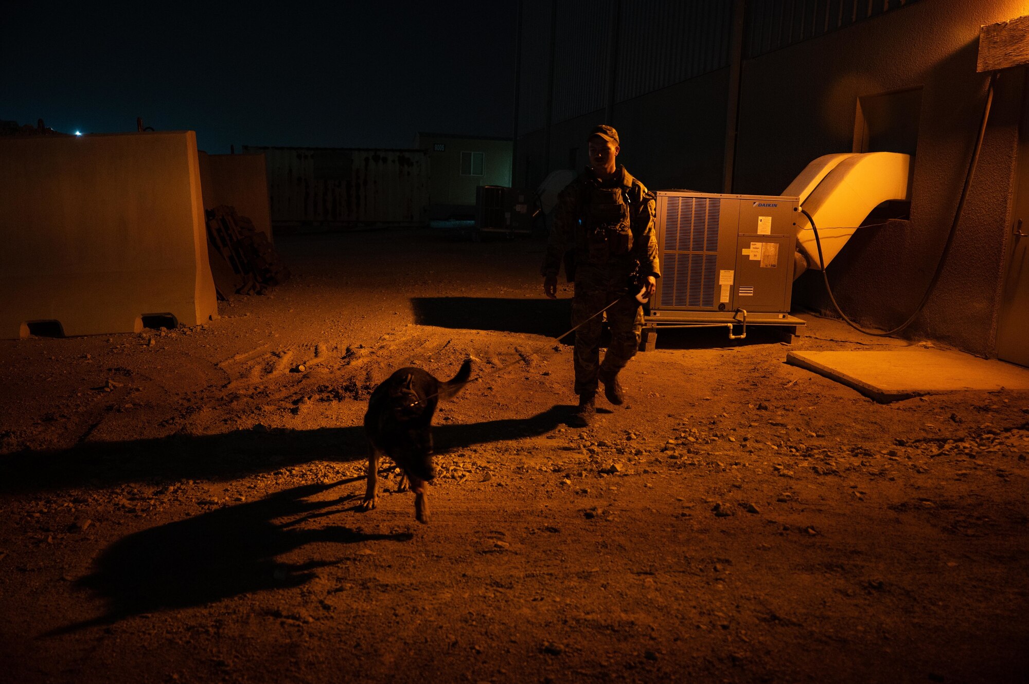 Military working dog handler, U.S. Air Force Staff Sgt. Justin Pickens of the 379th Expeditionary Security Forces Squadron, performs an evening detection patrol with his MWD around a building, at Al Udeid Air Base, Qatar, on AUG 10, 2022. Pickens has worked with five different MWD’s in his career and aspires to become a trainer someday. (U.S. Air Force photo by Staff Sgt. Dana Tourtellotte)