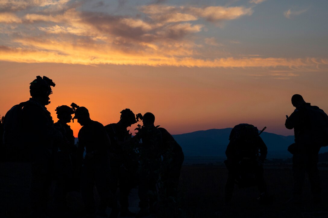 Foreign and domestic service members set up equipment for a training event at dusk.