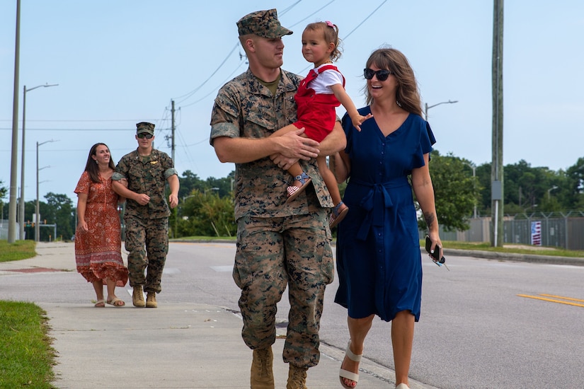 Two Marines, one holding a baby,  walk with their spouses along a road.