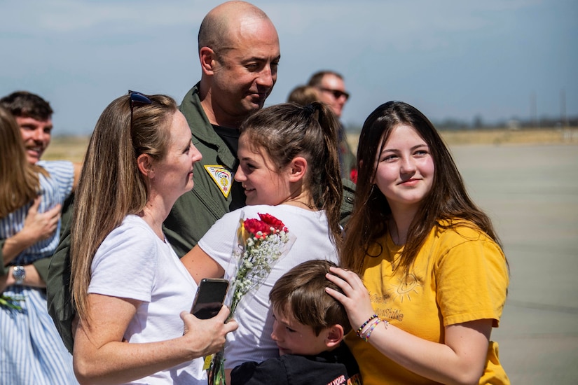 A sailor embraces four family members gathered around him.