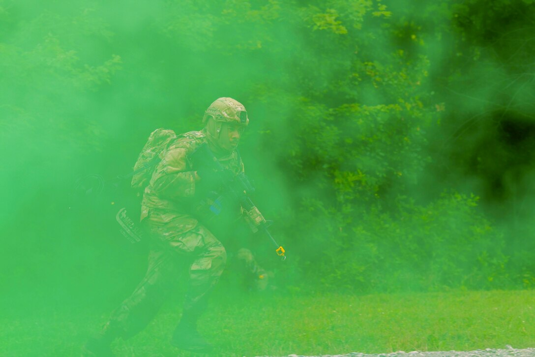 An airman carrying a weapon moves through green smoke in a field.