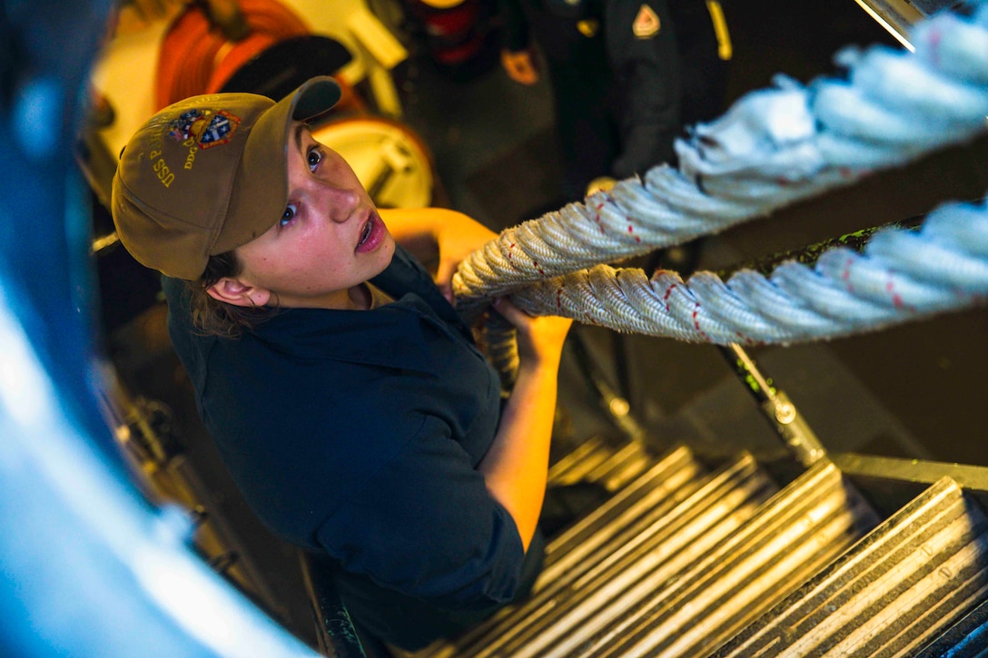 A sailor holds onto ropes in a compartment on a ship.