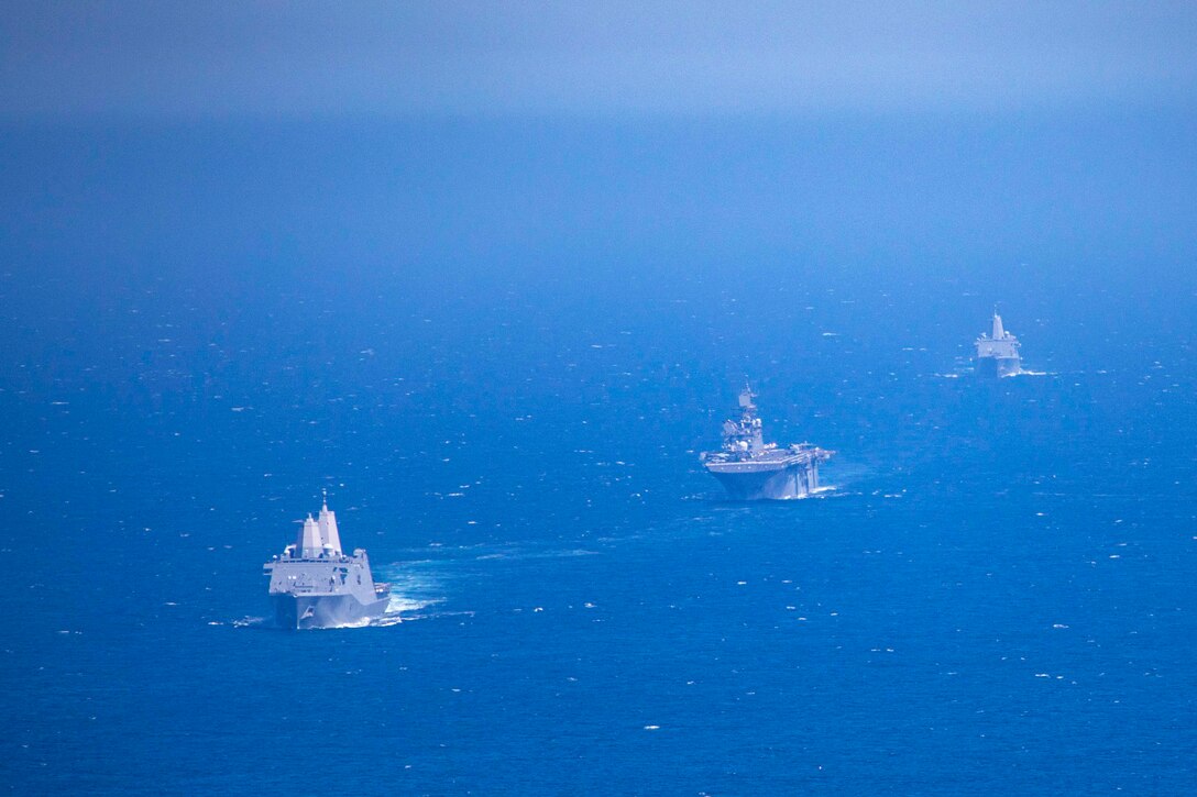 Three ships travel through waters in a line.