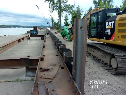 Steel beams line a pier going out into Little Sodus Bay with a yellow and black forklift to the right of the beams.