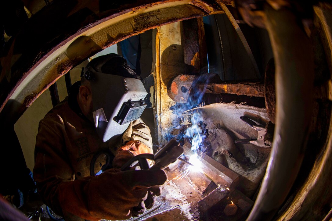 A sailor wearing a helmet welds a gate on a ship.