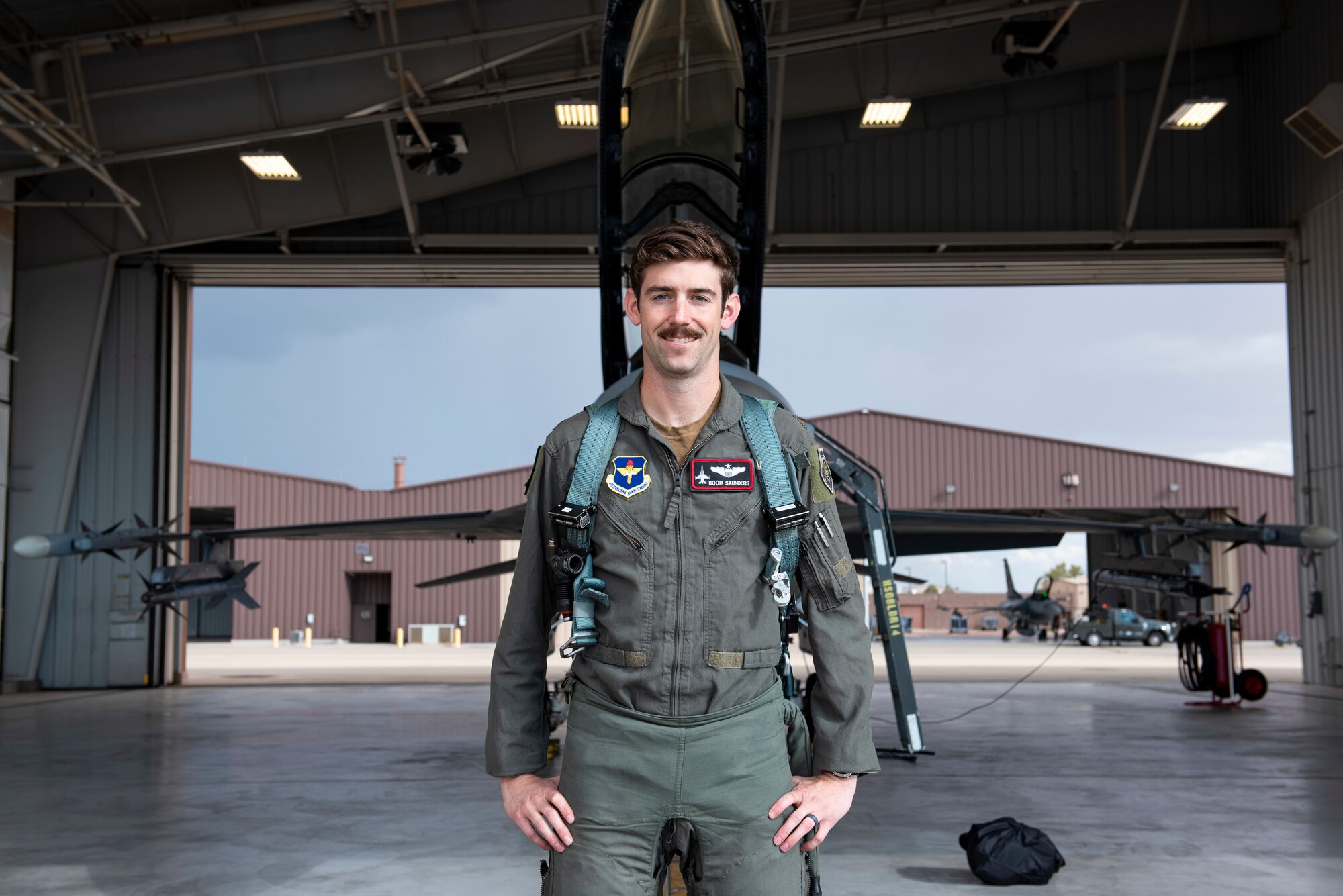 Major Benjamin Saunders in a flight suit poses in front of a grey F-16 Viper.