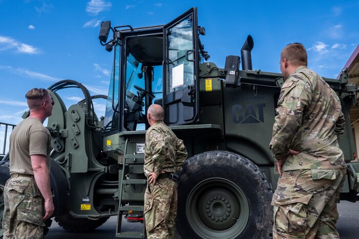 3 Royal Air Force Airmen stand outside of a giant vehicle.