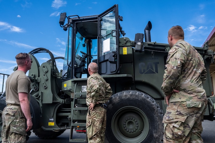 Royal Air Force Corp. Brian Bufton, middle, a movement technician assigned to the 4624th Air Movements Squadron at Royal Air Force Brize Norton, Oxfordshire, England, looks at a 10K Loader forklift vehicle at the Global Readiness Deployment Center on Travis Air Force Base, California, August 2, 2022. Bufton explained and experienced the similarities and differences between his job and U.S Air Force's aerial porter job with Airmen at Travis AFB. (U.S. Air Force photo by Staff Sgt. Scott Warner)