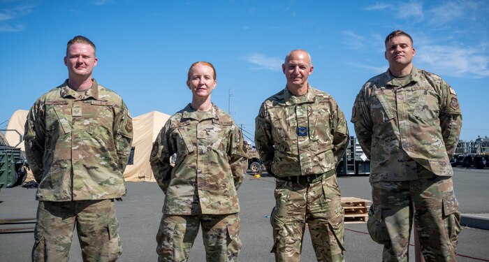 Royal Air Force Corp. Brian Bufton, second from right, a movement technician assigned to the 4624th Air Movements Squadron at Royal Air Force Brize Norton, Oxfordshire, England, poses for a photo with three Airmen at the Global Readiness Deployment Center on Travis Air Force Base, California, August 2, 2022. Bufton explained the similarities and differences between his job and U.S Air Force's aerial porter job with Airmen at Travis AFB. (U.S. Air Force photo by Staff Sgt. Scott Warner)