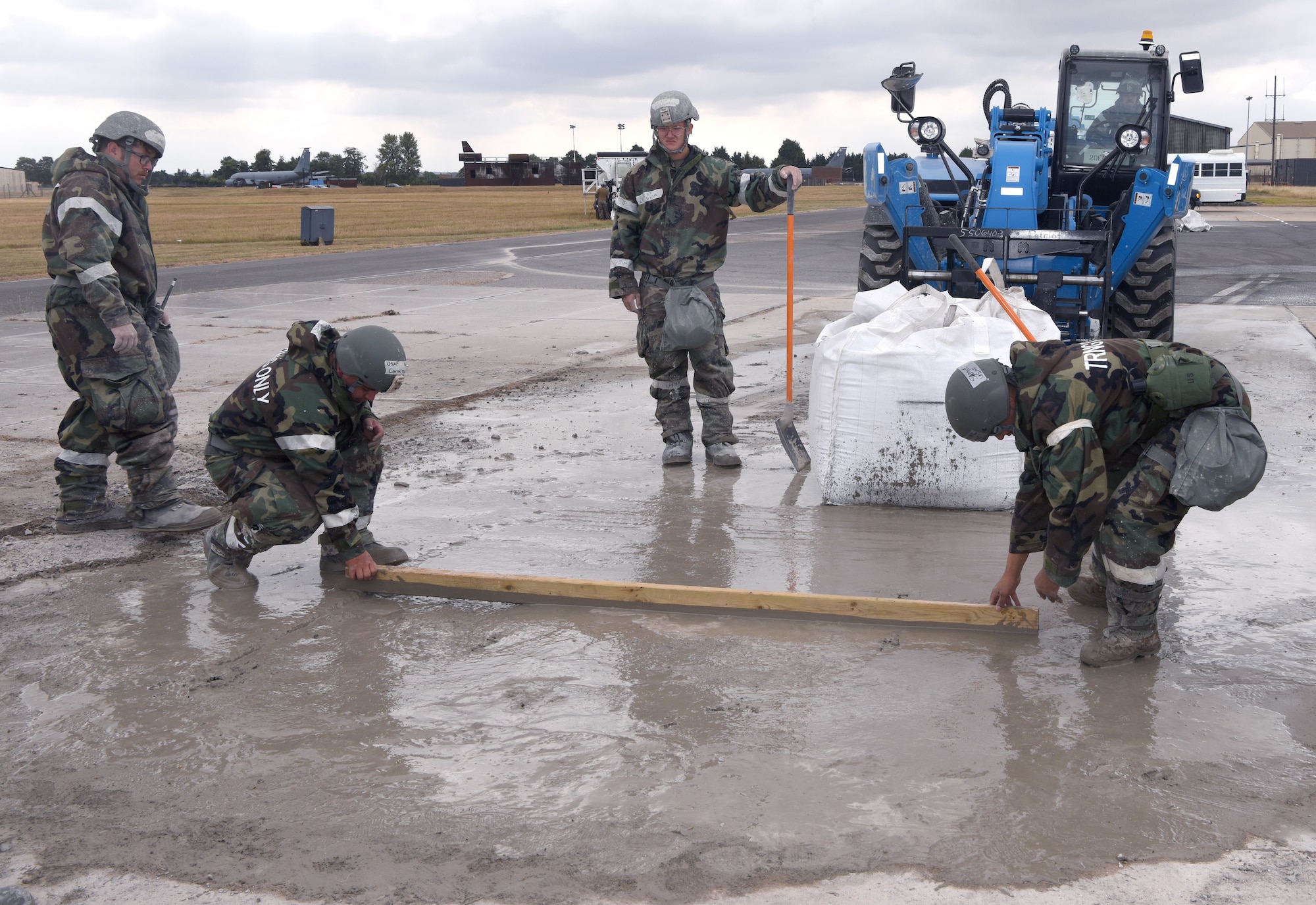 U.S. Air Force Airmen from the 100th Civil Engineer Squadron smooth fast-drying concrete as one of the final stages of a simulated damaged runway repair as part of a chemical, biological, radiological, nuclear and explosives exercise at Royal Air Force Mildenhall, England, Aug. 17, 2022. The 100th CES Airmen used a variety of equipment including excavators and loaders to practice removing damaged concrete and base course on a simulated runway. They practiced repair, break up and removal of concrete, before mixing and pouring new, quick-drying concrete and levelling it. (U.S. Air Force photo by Karen Abeyasekere)