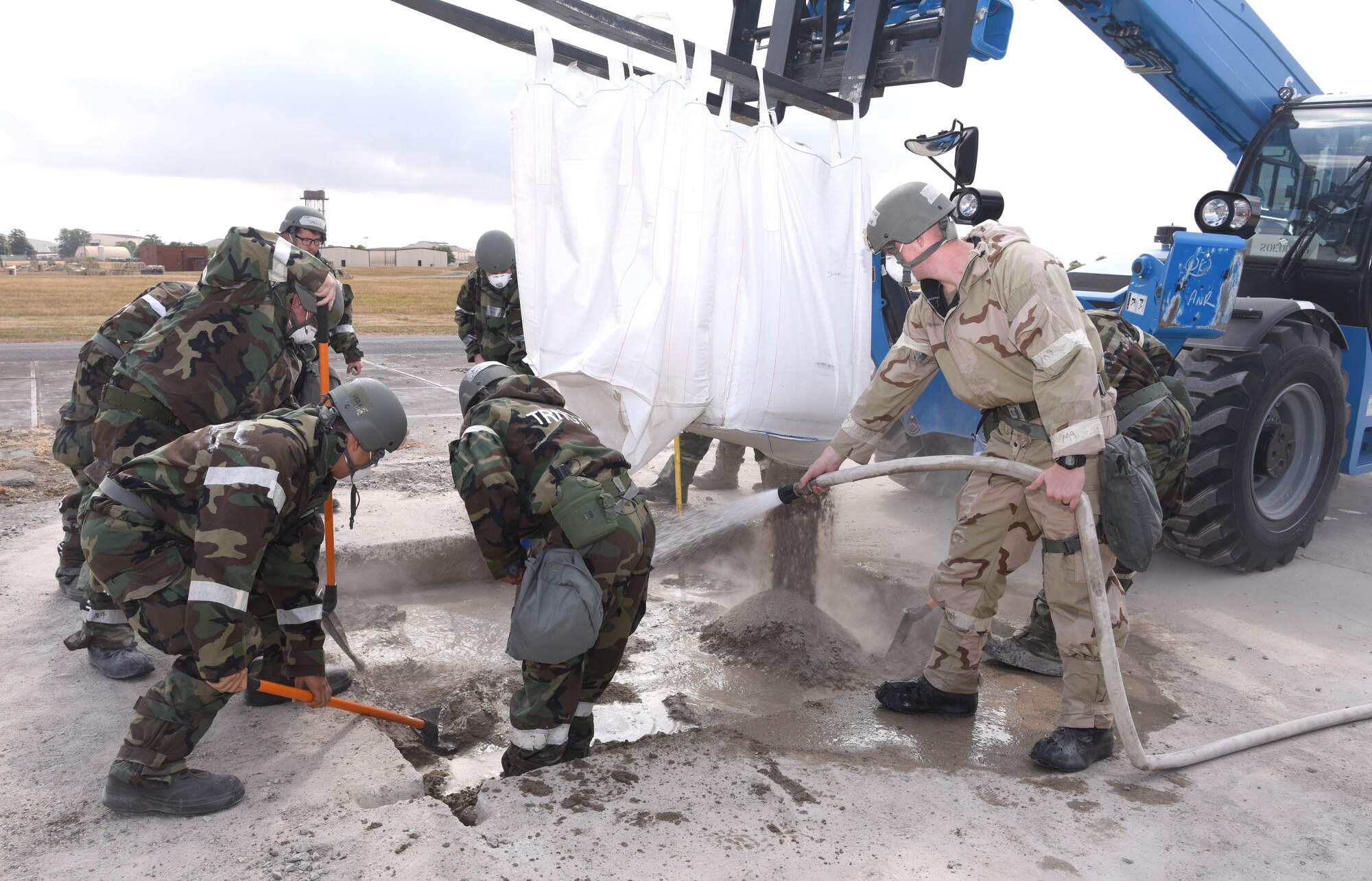 U.S. Air Force Airmen from the 100th Civil Engineer Squadron mix fast-drying concrete during a simulated damaged runway repair as part of a chemical, biological, radiological, nuclear and explosives exercise at Royal Air Force Mildenhall, England, Aug. 17, 2022. The 100th CES Airmen used a variety of equipment including excavators and loaders to practice removing damaged concrete and base course on a simulated runway. They practiced repair, break up and removal of concrete, before mixing and pouring new, quick-drying concrete and levelling it. (U.S. Air Force photo by Karen Abeyasekere)