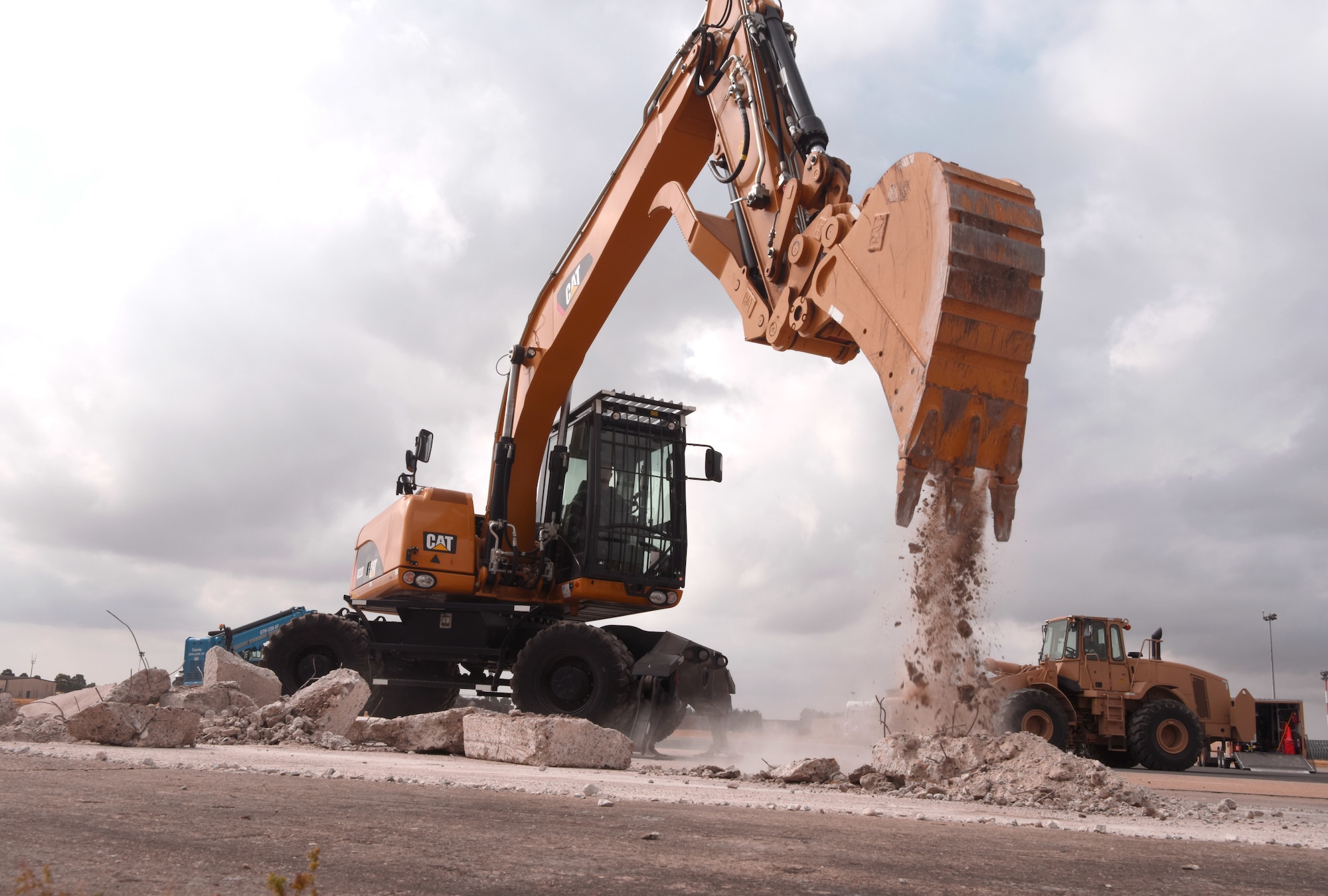 A U.S. Air Force 100th Civil Engineer Squadron Airman uses an excavator to clear concrete during a simulated runway repair as part of a chemical, biological, radiological, nuclear and explosives exercise at Royal Air Force Mildenhall, England, Aug. 17, 2022. The 100th CES Airmen used a variety of equipment including excavators and loaders to practice removing damaged concrete and base course on a simulated runway. They practiced repair, break up and removal of concrete, before mixing and pouring new, quick-drying concrete and levelling it. (U.S. Air Force photo by Karen Abeyasekere)