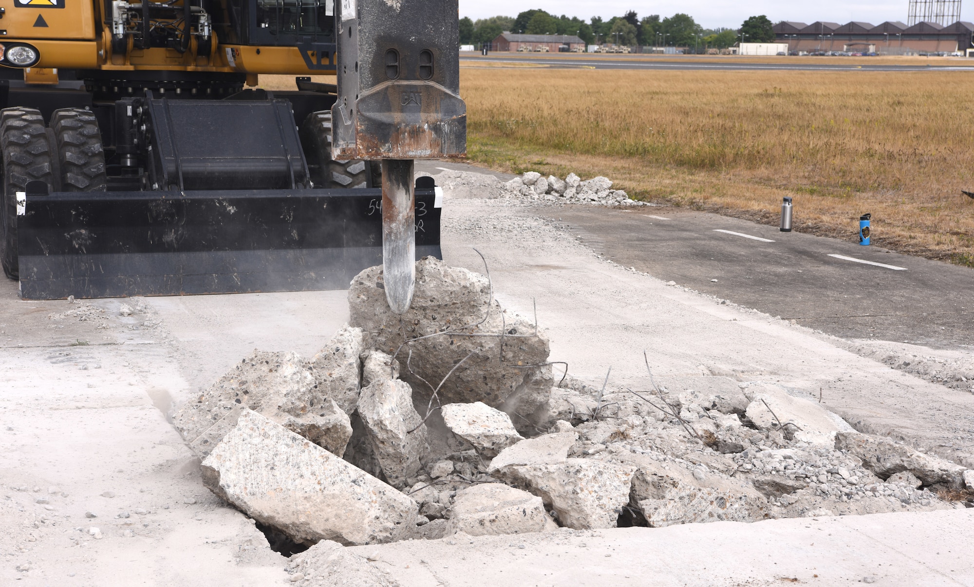 A U.S. Air Force 100th Civil Engineer Squadron Airman uses an excavator with a jackhammer to break up concrete during a simulated runway repair as part of a chemical, biological, radiological, nuclear and explosives exercise at Royal Air Force Mildenhall, England, Aug. 17, 2022. The 100th CES Airmen used a variety of equipment including excavators and loaders to practice removing damaged concrete and base course on a simulated runway. They practiced repair, break up and removal of concrete, before mixing and pouring new, quick-drying concrete and levelling it. (U.S. Air Force photo by Karen Abeyasekere)