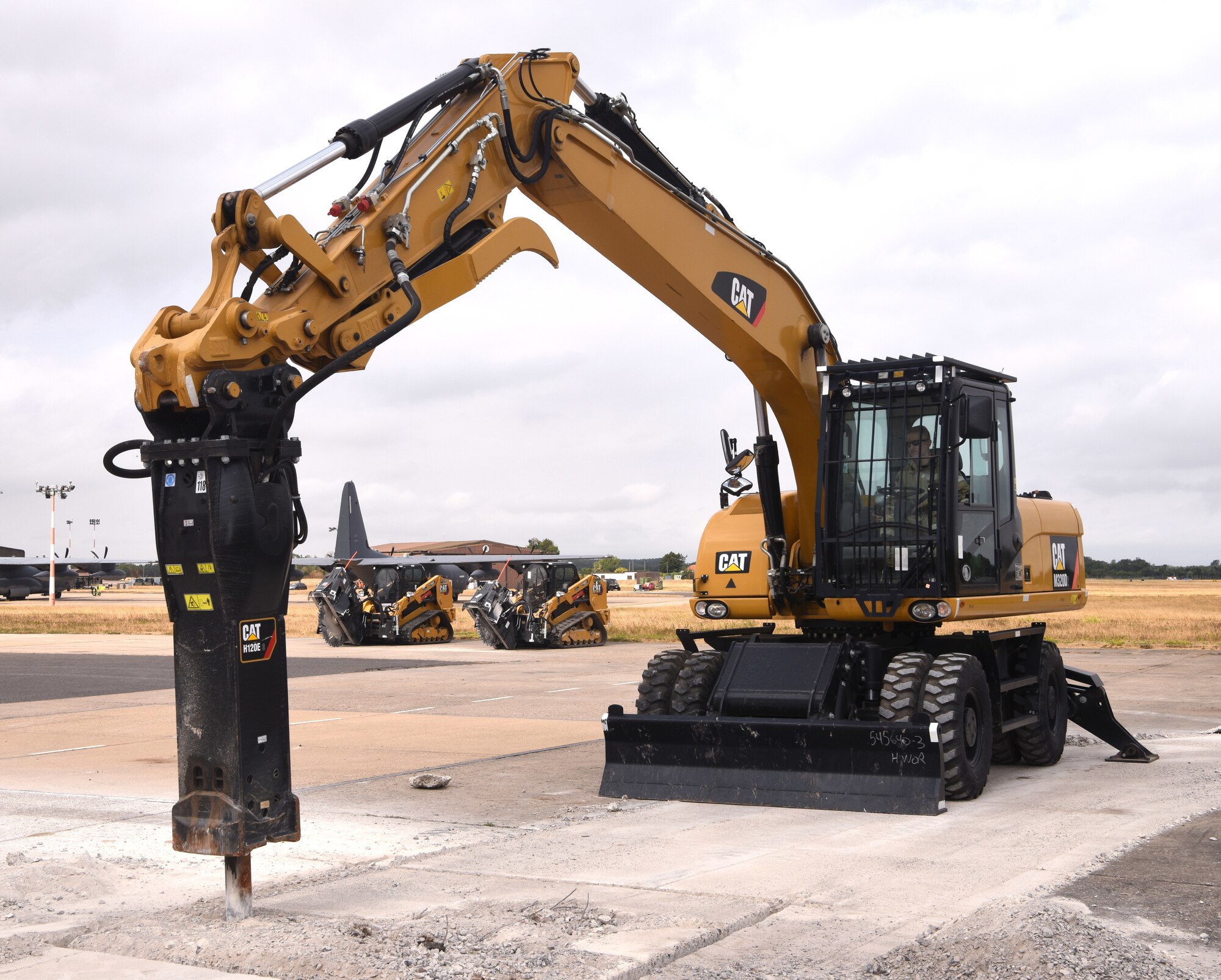 A U.S. Air Force 100th Civil Engineer Squadron Airman uses an excavator with a jackhammer to break up concrete during a simulated runway repair as part of a chemical, biological, radiological, nuclear and explosives exercise at Royal Air Force Mildenhall, England, Aug. 17, 2022. The Airmen used a variety of equipment including excavators and loaders to practice removing damaged concrete and base course on a simulated runway. They practiced repair, break up and removal of concrete, before mixing and pouring new, quick-drying concrete and levelling it. (U.S. Air Force photo by Karen Abeyasekere)
