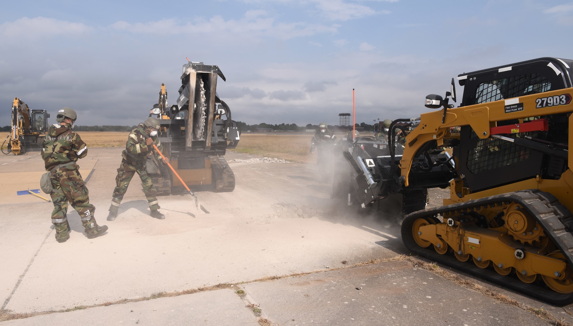 U.S. Air Force Airmen from the 100th Civil Engineer Squadron help clear broken concrete during a simulated runway repair as part of a a chemical, biological, radiological, nuclear and explosives exercise at Royal Air Force Mildenhall, England, Aug. 17, 2022. The Airmen used a variety of equipment including excavators and loaders to practice removing damaged concrete and base course on a simulated runway. They practiced repair, break up and removal of concrete, before mixing and pouring new, quick-drying concrete and levelling it, all while wearing mission-oriented protective postures gear. (U.S. Air Force photo by Karen Abeyasekere)