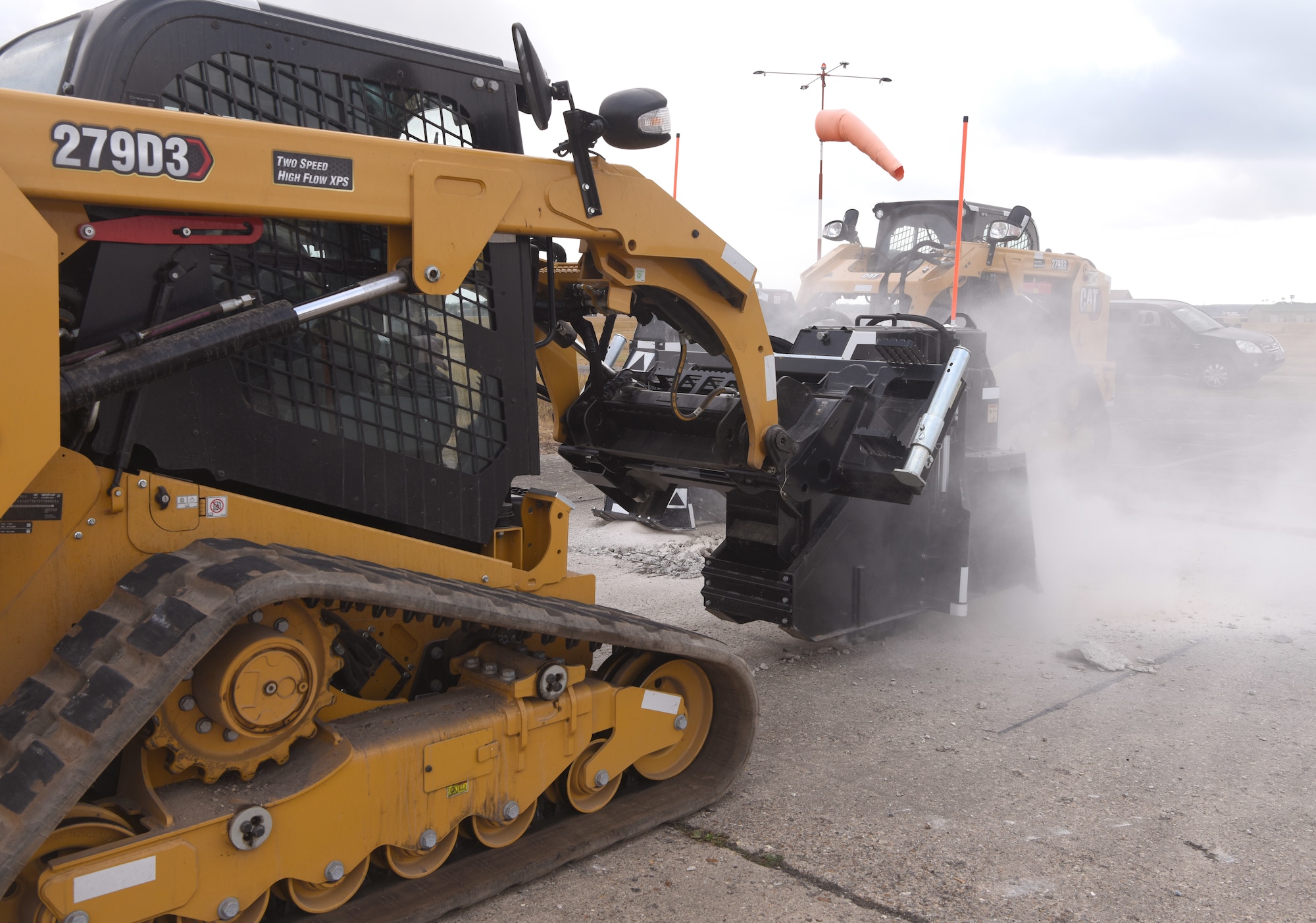 Two compact track loaders are used by Airmen from the 100th Civil Engineer Squadron to cut concrete during a chemical, biological, radiological, nuclear and explosives exercise at Royal Air Force Mildenhall, England, Aug. 17, 2022. The Airmen used a variety of equipment including excavators and loaders to practice removing damaged concrete and base course on a simulated runway. They practiced repair, break up and removal of concrete, before mixing and pouring new, quick-drying concrete and levelling it, all while wearing mission-oriented protective postures gear. (U.S. Air Force photo by Karen Abeyasekere)