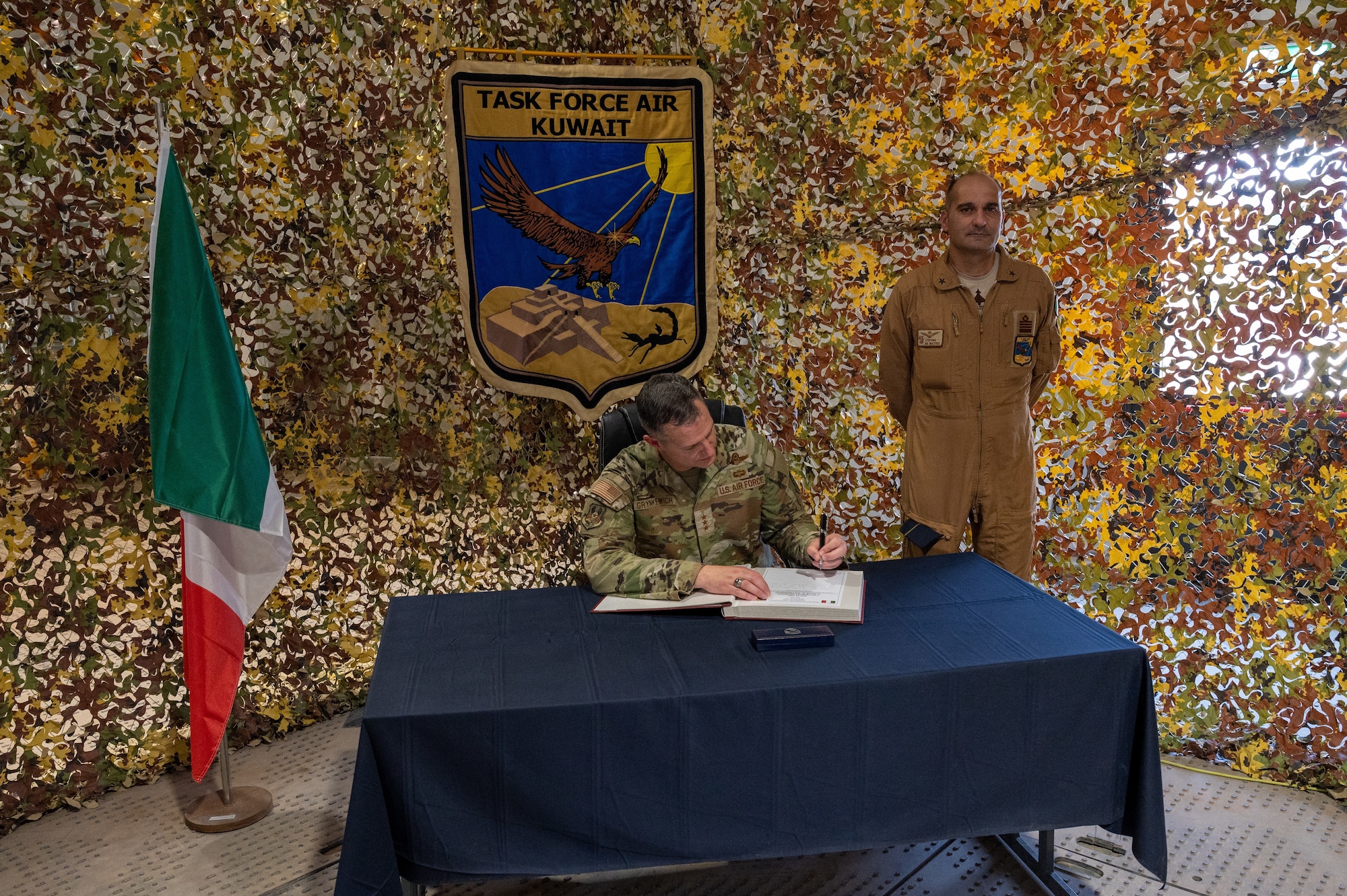 U.S. Air Force Lt. Gen. Alexus G. Grynkewich, center, Ninth Air Force (Air Forces Central) commander, signs the Italian Air Force base camp visitor log next to Stefano De Matteis, right, an IAF leader, at Ali Al Salem Air Base, Kuwait, Aug. 18, 2022. During the visit, Grynkewich met with Italian military members to discuss the importance of partner nation integration within the U.S. Central Command area of responsibility. (U.S. Air Force photo by Senior Airman Dominic Tyler)