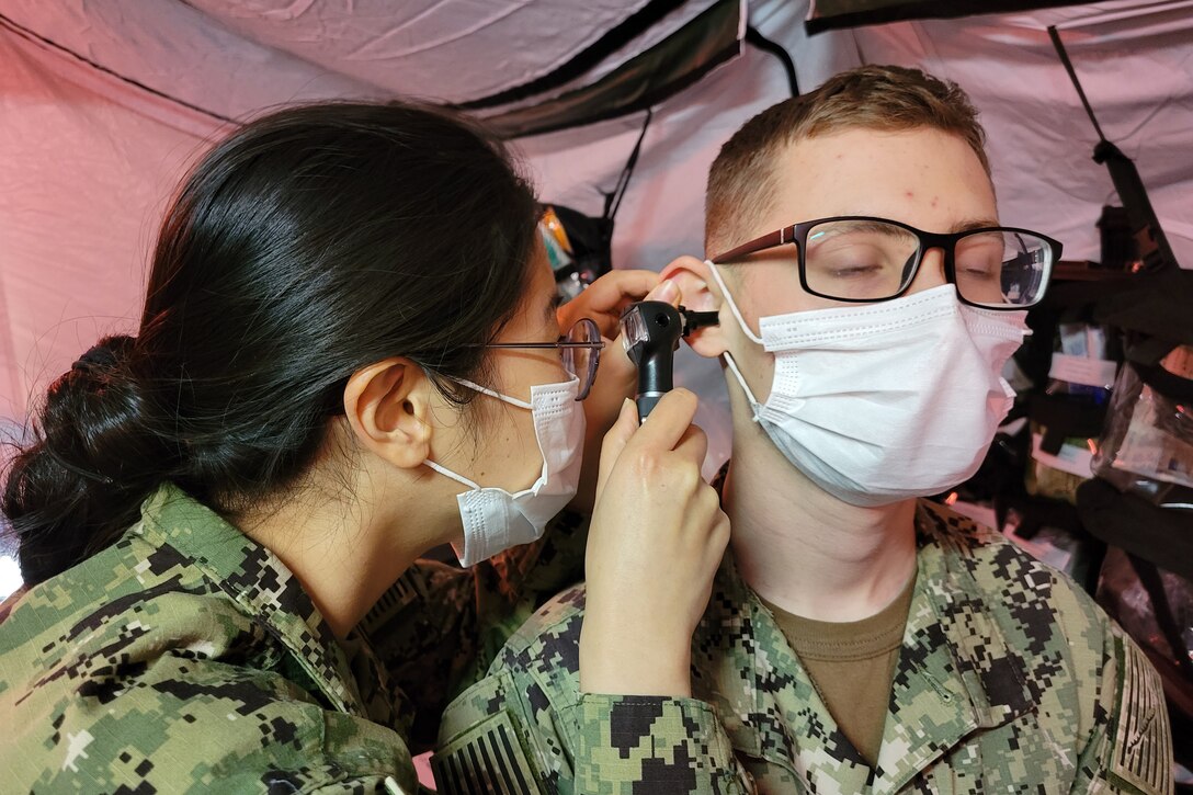 A sailor examines the inside of another sailor's ear.