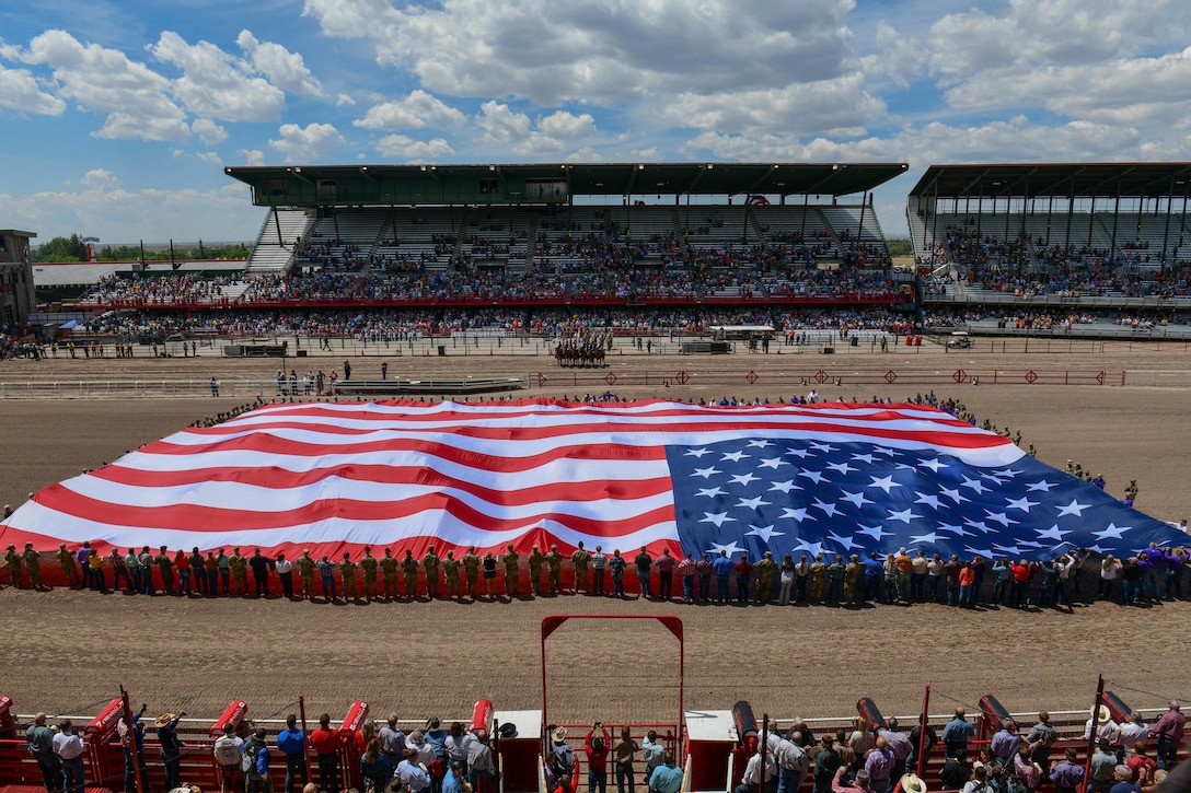 Airmen and their families hold a giant American flag in a large stadium.