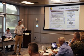 PENSACOLA, Fla. (Aug. 17, 2022) Ryan Dallett, a program analyst in the Naval Education and Training Command (NETC) strategy, innovation, and voluntary education N5 directorate, explains the elements of a strategic planning framework with NETC headquarters leaders during the NETC Force Development fiscal year 2023 strategic offsite Aug. 17, 2022.  Senior members of the staff came together to discuss NETC’s mission and vision statements and refine strategic goals and objectives and annual goals. (U.S. Navy photo by Wade Buffington)