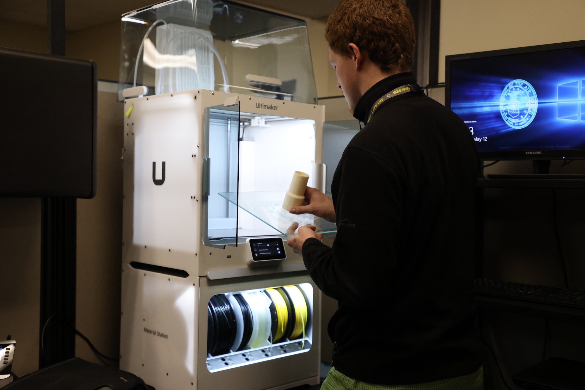 Zachary Coulson, 76th Aircraft Maintenance Group mechanical engineer, stands in front of 3D printer removing a newly printed component.
