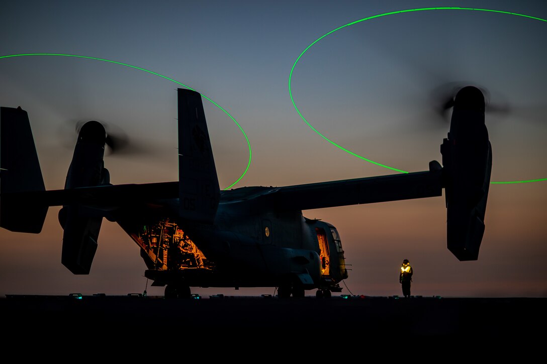 An MV-22 Osprey sits on the flight deck of a ship at night.