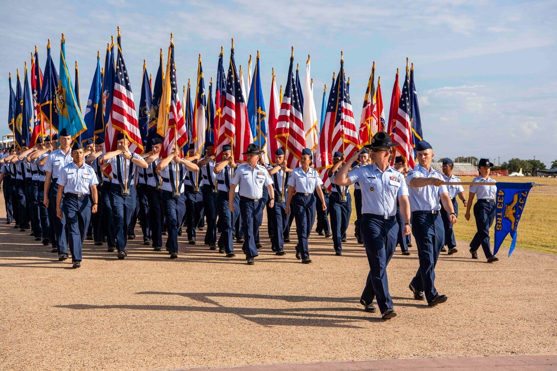 A group of airmen march in formation while holding flags.