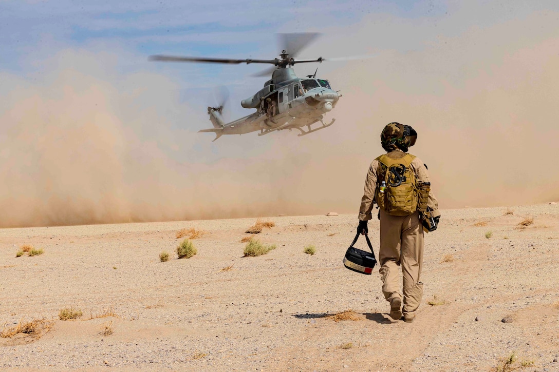 A Marine walks toward an airborne helicopter.