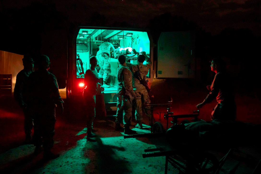 Soldiers stand in around an ambulance at night.