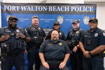 Six police officers in uniform stand in front of a police-department-branded backdrop