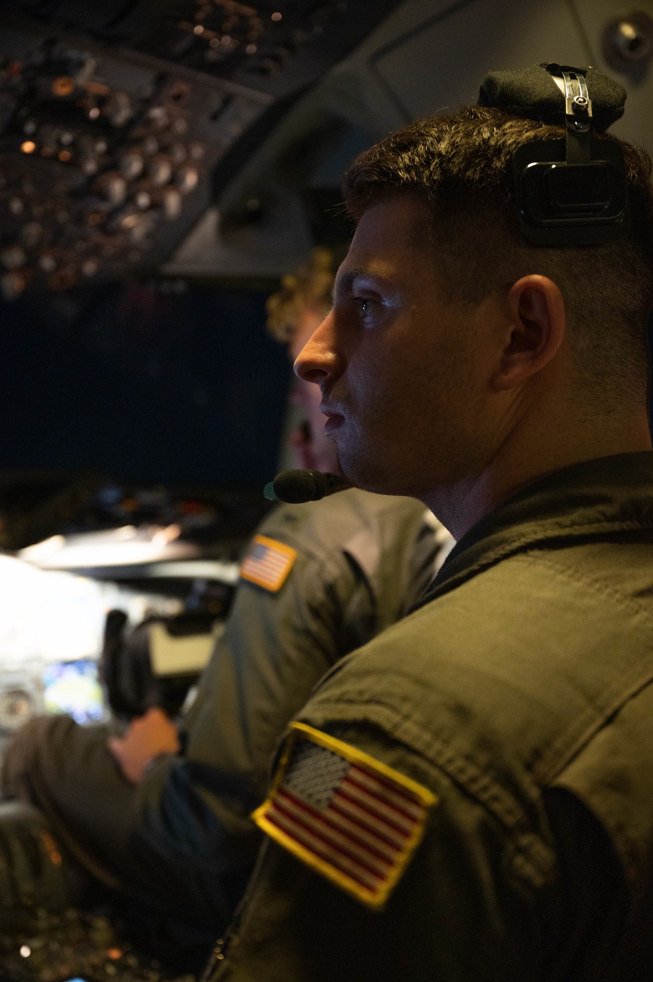 An Airman sits in the cockpit of an aircraft with a headset on.