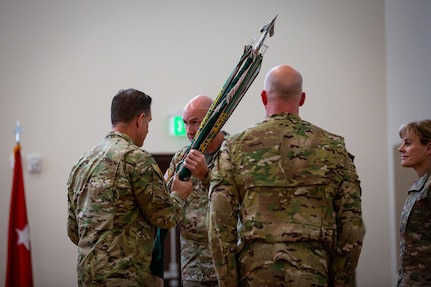 Four soldiers face each other and pass a flag to each other.