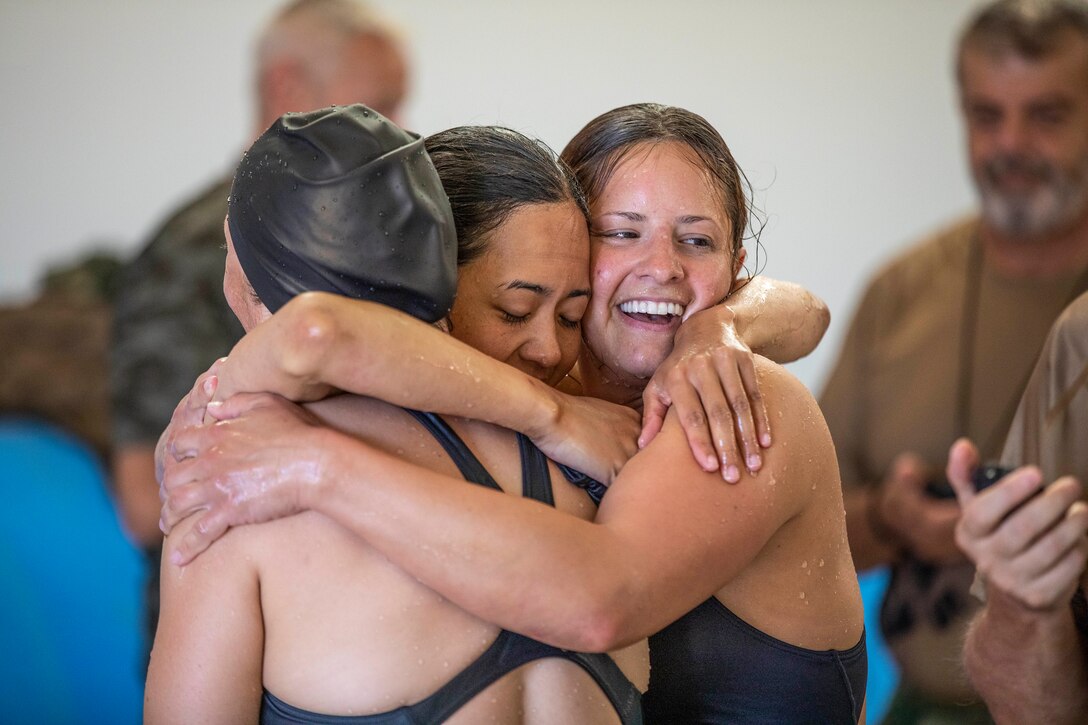 Three athletes in swimsuits embrace.