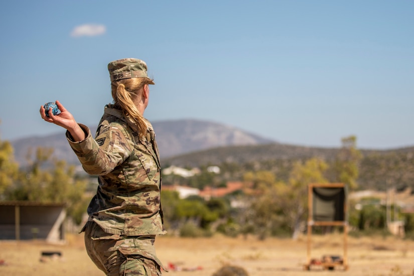 A soldier shown from behind brings her arm before throwing a projectile outside.