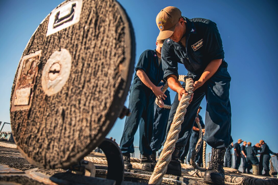 A sailor stows away a line on the flight deck of a ship.